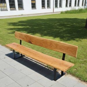 Hochwertige Gartenbank mit Rückenlehne aus massiver Eiche auf einer grauen Steinterrasse vor einem weißen Gebäude mit englischem Rasen.