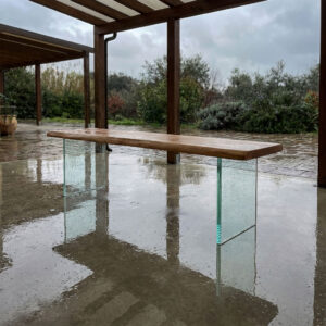 Eichenbank mit Glasuntergestell auf überdachter Terrasse bei Regen mit Reflexionen