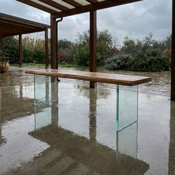 Eichenbank mit Glasuntergestell auf überdachter Terrasse bei Regen mit Reflexionen